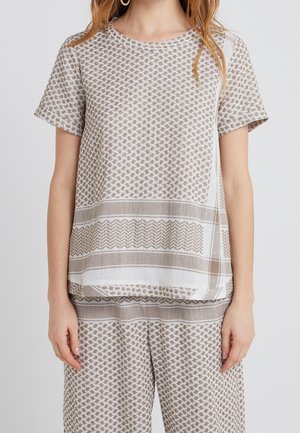 Femme portant un haut à manches courtes beige et blanc à motifs et un pantalon ample assorti sur un fond uni.