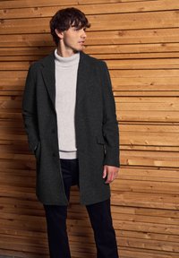 Tmavě šedý vlněný kabát s upraveným střihem, s jedním knoflíkovým zapínáním a bočními kapsami, vrstvený přes světle šedý rolák a námořnické kalhoty.