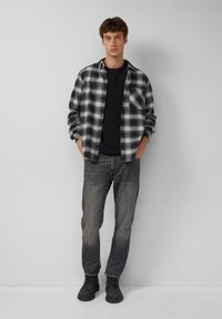 Zwart-wit geruite flanellen overhemd over een zwart T-shirt, gecombineerd met vervaagde grijze jeans en donkere schoenen. Eenvoudig ontwerp met een ontspannen pasvorm.
