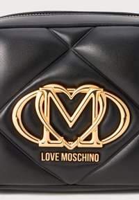 Bolsa de ombro em pele sintética acolchoada preta, apresentando um logótipo em metal dourado com letras entrelaçadas "M" e "O" e o nome da marca "LOVE MOSCHINO" abaixo.