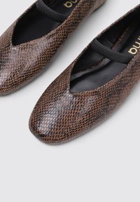Ballerines marron à motif serpent avec une finition mate, dotées d'un design découpé et d'une sangle élastique noire sur le cou-de-pied.