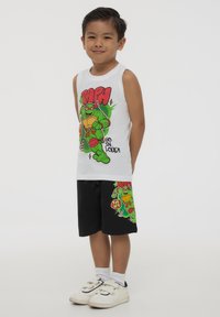 Maglietta bianca senza maniche con grafica di personaggio dei cartoni animati verde e testo; pantaloni corti neri con un design di personaggio simile. Abbigliamento casual in cotone.