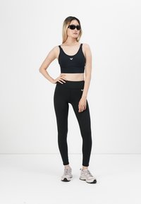 Svart sports BH og høyt liv leggings laget av elastisk stoff. Antrekket har et minimalistisk design og en liten logo på toppen.