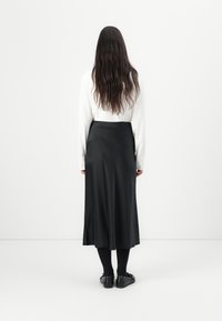 Schwarzer Satinrock mit glatter Textur, der bis zur Mitte der Wade reicht. Kombiniert mit einem weißen Langarmhemd, schwarzen Socken und flachen Schuhen.