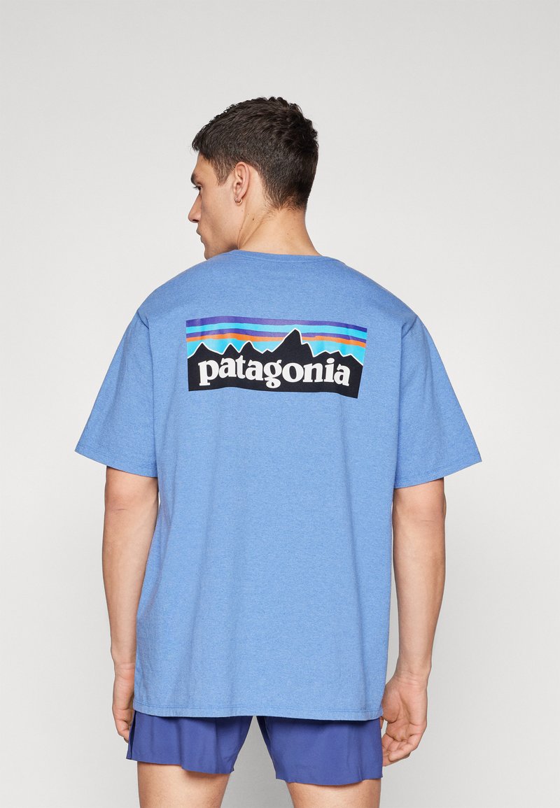 Tricou din bumbac albastru, cu o croială lejeră. Prezintă un logo negru Patagonia cu grafica munților și dungi orizontale colorate pe spate.