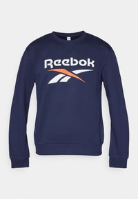 Tmavomodrá mikina vyrobená z bavlny s okrúhlym výstrihom, na prednej strane s veľkým bielym a oranžovým logom Reebok. Ramená a spodný lem sú ribbované.