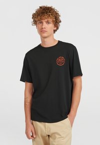 Black cotton t-shirt with short sleeves, round neck, and a circular orange graphic print on the left chest. Casual fit and smooth texture.