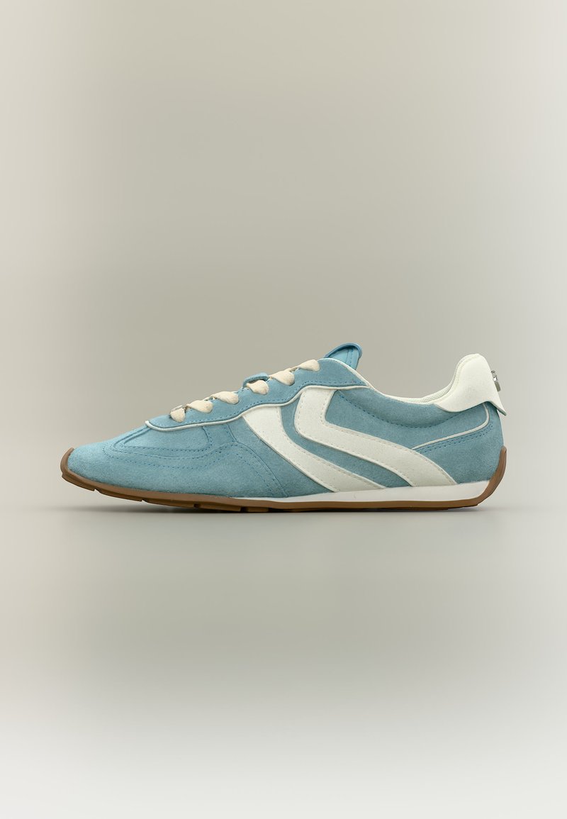 Αθλητικό παπούτσι από γαλάζιο σουέντ με λευκές ρίγες σε σχήμα σήμανσης, εκρού κορδόνια, λευκή ταμπέλα στη φτέρνα και καφέ σόλα, πλευρική όψη σε ουδέτερο φόντο.