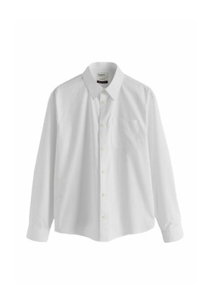 Mains boutonnant le poignet d'une chemise blanche portée avec un pantalon gris à fines rayures.