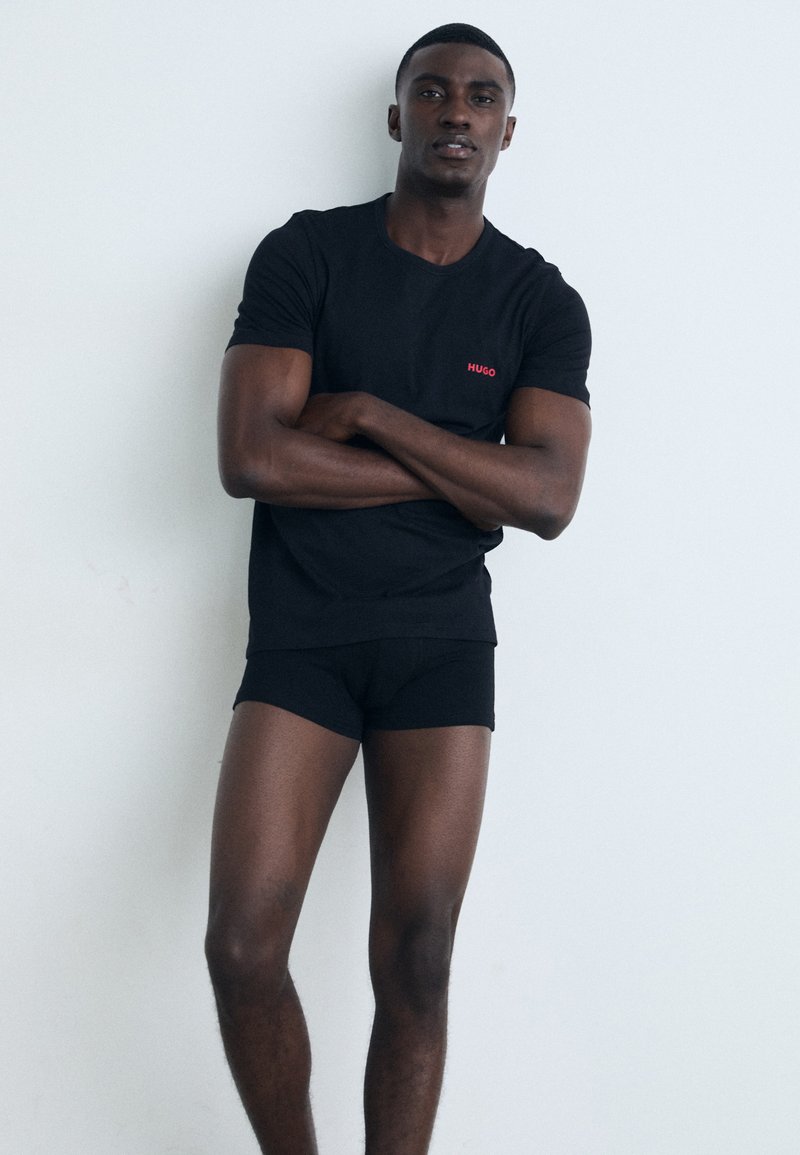 T-shirt noir avec un logo "HUGO" rouge, associé à des boxers noirs. Les vêtements sont ajustés et ont une texture lisse.