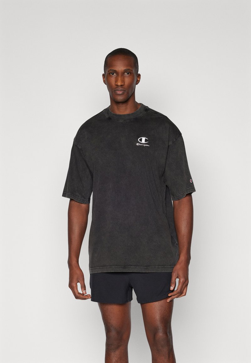 Schwarz oversized T-Shirt mit kurzen Ärmeln aus bequemem Stoff, mit einem kleinen weißen Logo auf der Brust und einem lockeren Schnitt.
