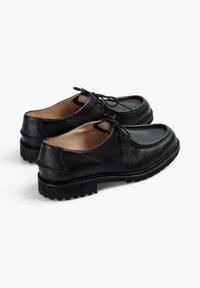 Zapatos de cuero negro con un acabado texturizado, diseño de cordones y suelas de goma resistentes con un patrón de relieve pronunciado.