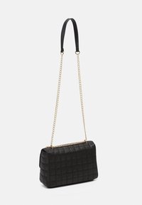 Borsa a mano nera trapuntata di forma rettangolare, con una tracolla in catena dorata e un manico in pelle nera liscia. Dettagli della superficie texture visibili.