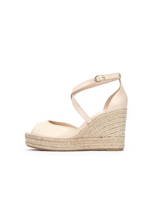 Sandales compensées beiges à bout ouvert, avec un design à lanières croisées et un détail de boucle. Plateforme en jute et semelle texturée.