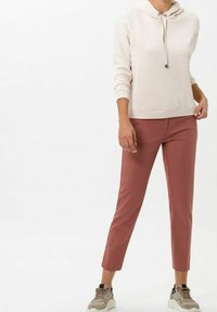 Light pink hoodie with a drawstring hood and ribbed cuffs, paired with fitted dusty rose pants. Model wears beige sneakers.