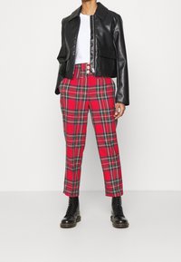 Svart fusk läder kort jakke med två framfickor, kombinerat med röda rutiga byxor med gröna och svarta linjer. Svarta ankellånga stövlar.