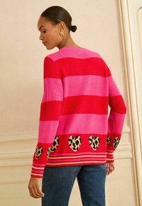 Pehme anyagból készült rózsaszín és piros csíkos pulóver, amelynek alján leopárdmintás szív díszíti, és bordázott mandzsettái vannak.