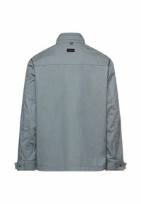 Lysegrå langærmet jakke med ståkrave, knaplukning ved ærmekanterne og et lille sort rektangulært mærke øverst på ryggen.