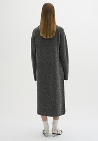 Cappotto lungo in lana grigia con una vestibilità rilassata e spalle cadute, caratterizzato da un design di lunghezza intermedia e una texture minimalista.