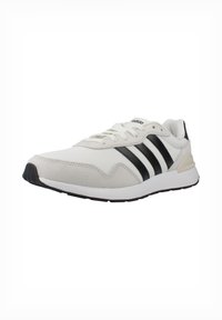 Zapatilla deportiva blanca con acentos en negro con tres franjas, parte superior de malla y suela de goma. Presenta lengüeta y cuello acolchados para mayor comodidad.