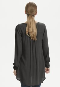 Blusa nera a maniche lunghe in tessuto leggero e testurizzato. Presenta una schiena plissettata, scollatura rotonda e orlo arrotondato.