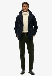 Marineblå uld peacoat med dobbeltknaplukning, cremefarvet turtleneck, olivengrønne bukser og sorte læderstøvler. Minimalistisk design, struktureret pasform.