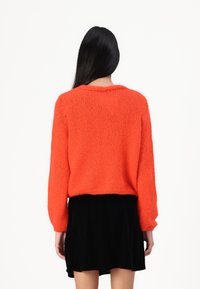 Un pull en tricot orange vif avec des manches longues, un col rond et un ourlet côtelé, assorti à une jupe en velours noire.