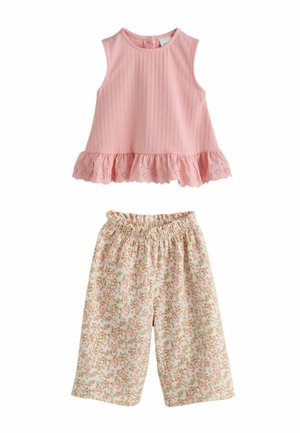 Różowy top bez rękawów z falbaną u dołu w połączeniu z białymi spodniami o szerokich nogawkach, zdobionymi drobnym różowo-zielonym kwiatowym nadrukiem.