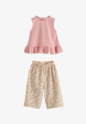 Ujjatlan rózsaszín felső fodros szegéllyel, fehér, bő szárú nadrággal párosítva, amelyen apró rózsaszín és zöld virágminta található.