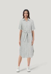 Vestito a camicia a righe in bianco e verde, con vita afferrata da una cintura, maniche corte e spacchi laterali. Realizzato in tessuto leggero.