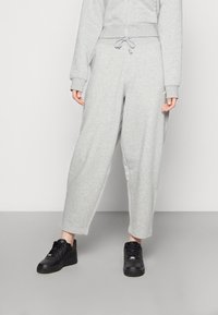 Lys grå joggebukser laget av mykt stoff, med avslappet passform, elastisk midje med snøring og sidelommer. Kombinert med svarte joggesko.