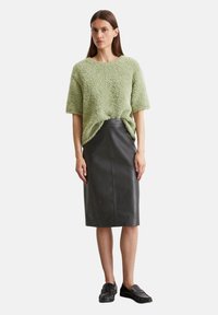 Mintgrüner strukturierter Pullover, kurzärmlig, kombiniert mit einem schwarzen Lederröckchen. Schwarze Slipper runden das Outfit ab.