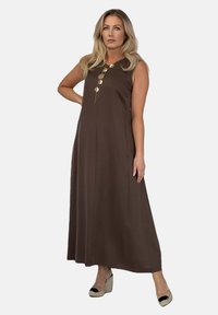 Brązowa, bezrękawnikowa sukienka maxi z przodem zapinanym na guziki, gładki materiał, luźny krój, w połączeniu z butami na koturnie z espadryli.