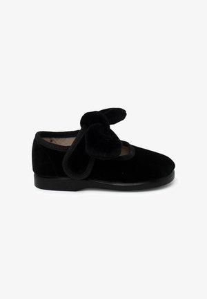 Scarpa di velluto nero con punta arrotondata, suola in gomma e un fiocco decorativo sulla parte frontale. I bordi rifiniti esaltano la sua morbidezza.