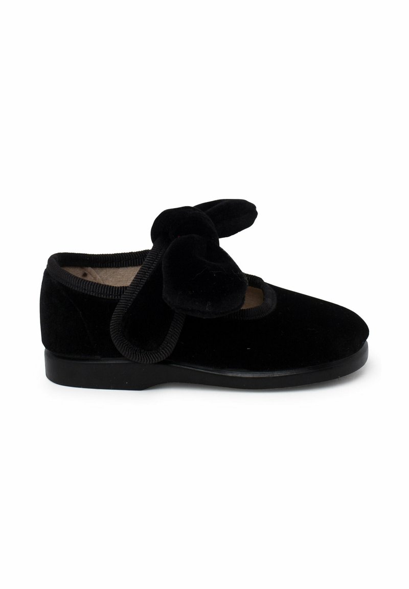 Zapato de terciopelo negro con punta redondeada, suela de goma y un lazo decorativo en la parte delantera. Los bordes terminados realzan su textura suave.