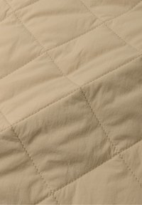 Beige quilted comforter with a soft texture, featuring stitched squares for a patterned design. Material appears lightweight and smooth.
