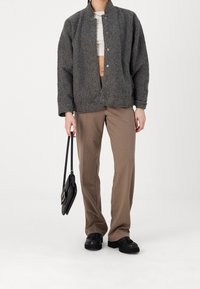 Grå ullblandad jacka med hög krage, framsnappstängning och sänkta axlar, parat med beige raka byxor och en svart väska.