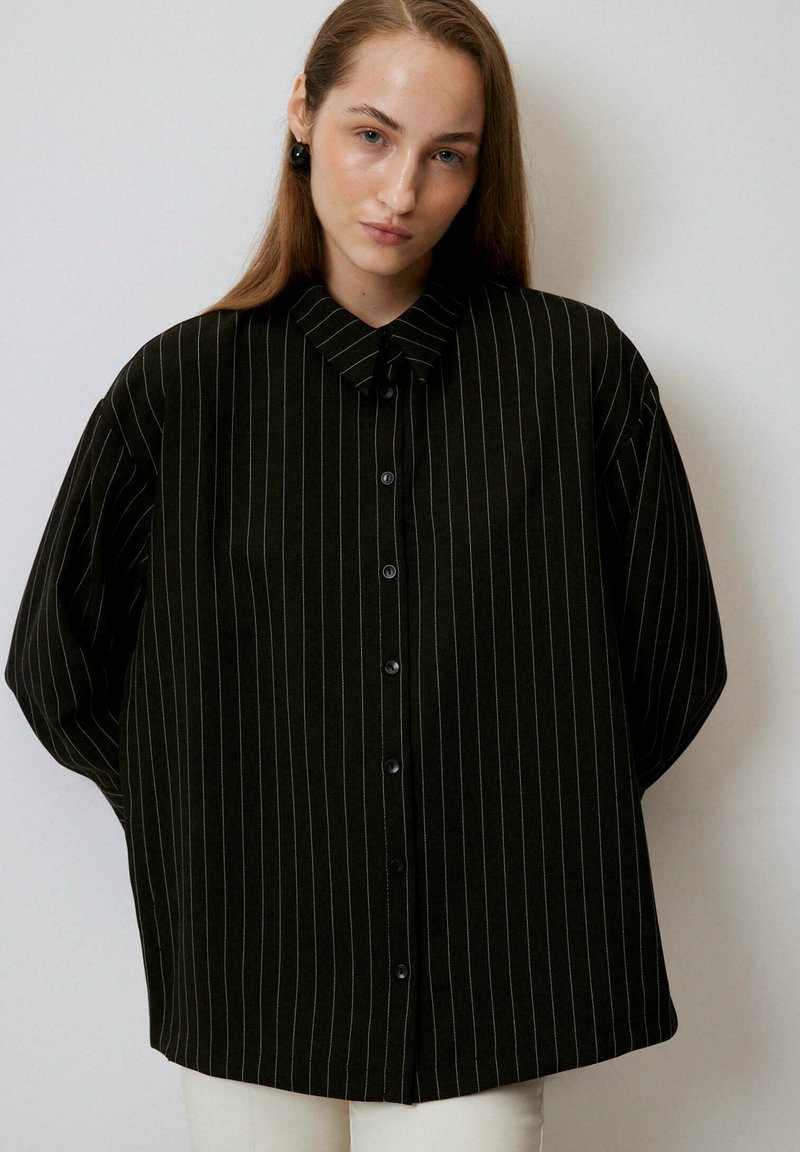 Dark green oversized button-up shirt featuring vertical white stripes, a classic collar, and relaxed sleeves. Smooth fabric with slight sheen.