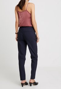 Skriftligt navybyxor med en jämn textur, som har sidofickor och smalnande ben, kombinerat med en ärmlös bourgogneröd topp.