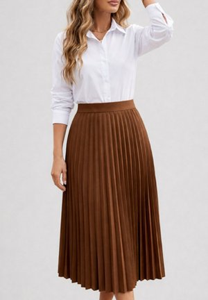 Femme portant une chemise blanche à manches longues rentrée dans une jupe midi plissée marron taille haute, debout devant un fond neutre.