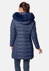 Abrigo acolchado azul marino con capucha de piel sintética, que presenta un diseño acolchado y un corte de longitud media. Las mangas son ligeramente ajustadas y suaves.