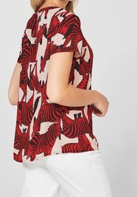 Röd och svart blus med zebramönster i lätt tyg, korta ärmar och löst snitt, med rund halsringning och asymmetrisk nederkant.