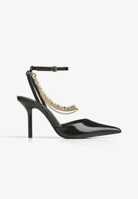 Črne lakk kožne ženske čevlje s koničastim nosom, stiletto peto in gležnjsko zanko, okrašeno z zlatimi verigami. Gladka tekstura po vsej površini.