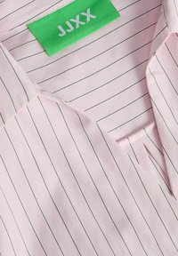 Heleroosa triiksärk õhukeste tumedate vertikaalsete triipudega, millel on kaeluse sees roheline silt, millel on märgistus "JJXX".