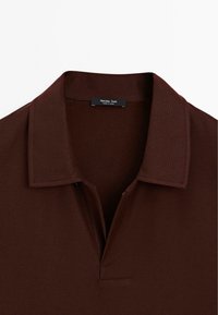 Mörkbrun polo skjorta med en texturerad väv, med krage och en fyrdelad dragkedja. Märket "Massimo Dutti" står på insidan av halsen.
