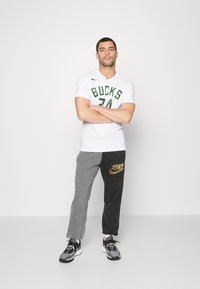 Hvid t-shirt med "BUCKS" og nummer 74 i grøn; grå og sorte sweatpants med guld Nike-logo; sorte og grå træningssko.