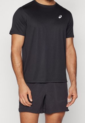 Homme portant un maillot de sport noir à manches courtes et un short assorti, debout les bras détendus le long du corps.