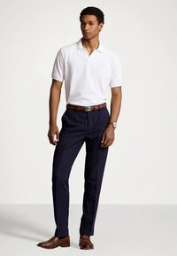 Λευκό πόλο πουκάμισο, μπλε παντελόνι με λεπτές ρίγες, καφέ δερμάτινη ζώνη και παπούτσια. Φαρδιά εφαρμογή, απαλό ύφασμα, κοντά μανίκια και κλασικός γιακάς.