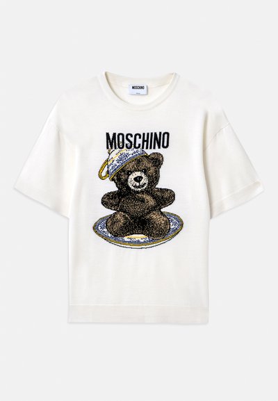 T-shirt bianca a maniche corte con una grafica di un orso nero su un piatto decorativo blu. "Moschino" stampato sopra il design in nero. Tessuto morbido.