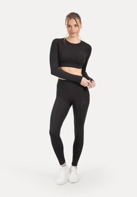 Top corto atletico nero e leggings a vita alta realizzati in materiale elastico, con design aderente e maniche lunghe.
